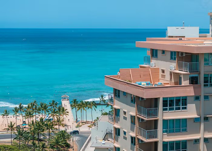 Oceanfront view of Queen Kapiolani Hotel Waikiki with turquoise beach and palm trees